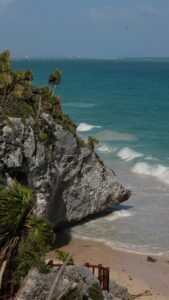 Beautiful view of Tulum's beach and cliffs in Mexico, featuring turquoise blue sea and palm trees.