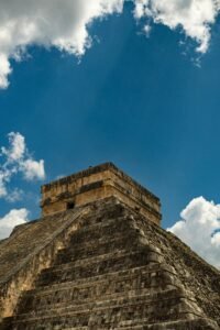 Low angle view of Chichén Itzá pyramid against a bright blue sky with clouds.